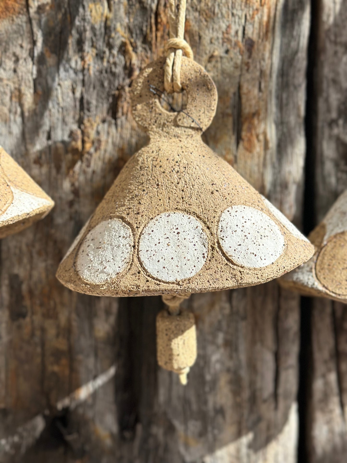 Handmade stoneware bell with gritty whitewashed surface and circular motif, suspended by flax fibre rope