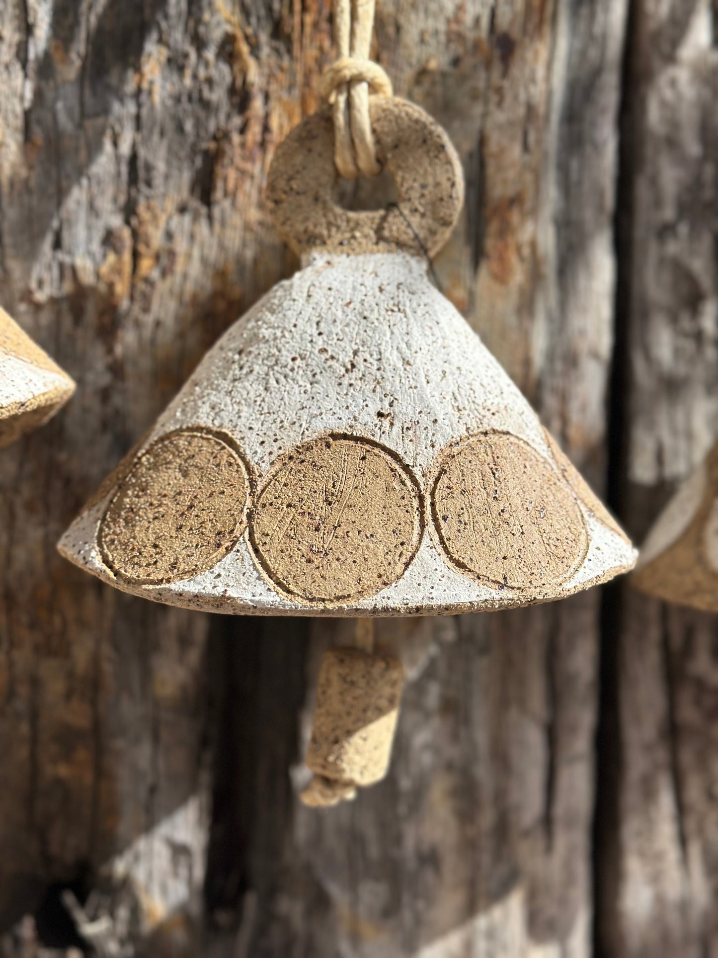 Handmade stoneware bell with gritty whitewashed surface and circular motif, suspended by flax fibre rope
