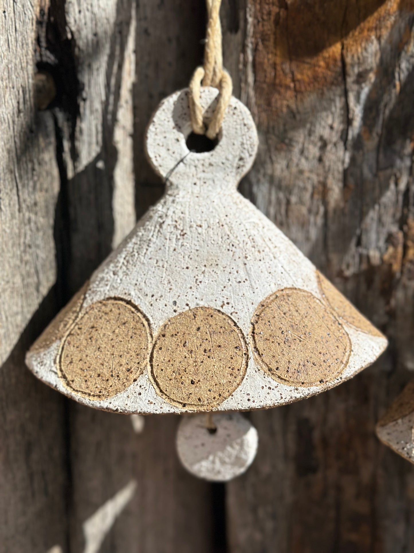 Textured stoneware bell form with subtle mid-century modern patterning, hanging against timber backdrop