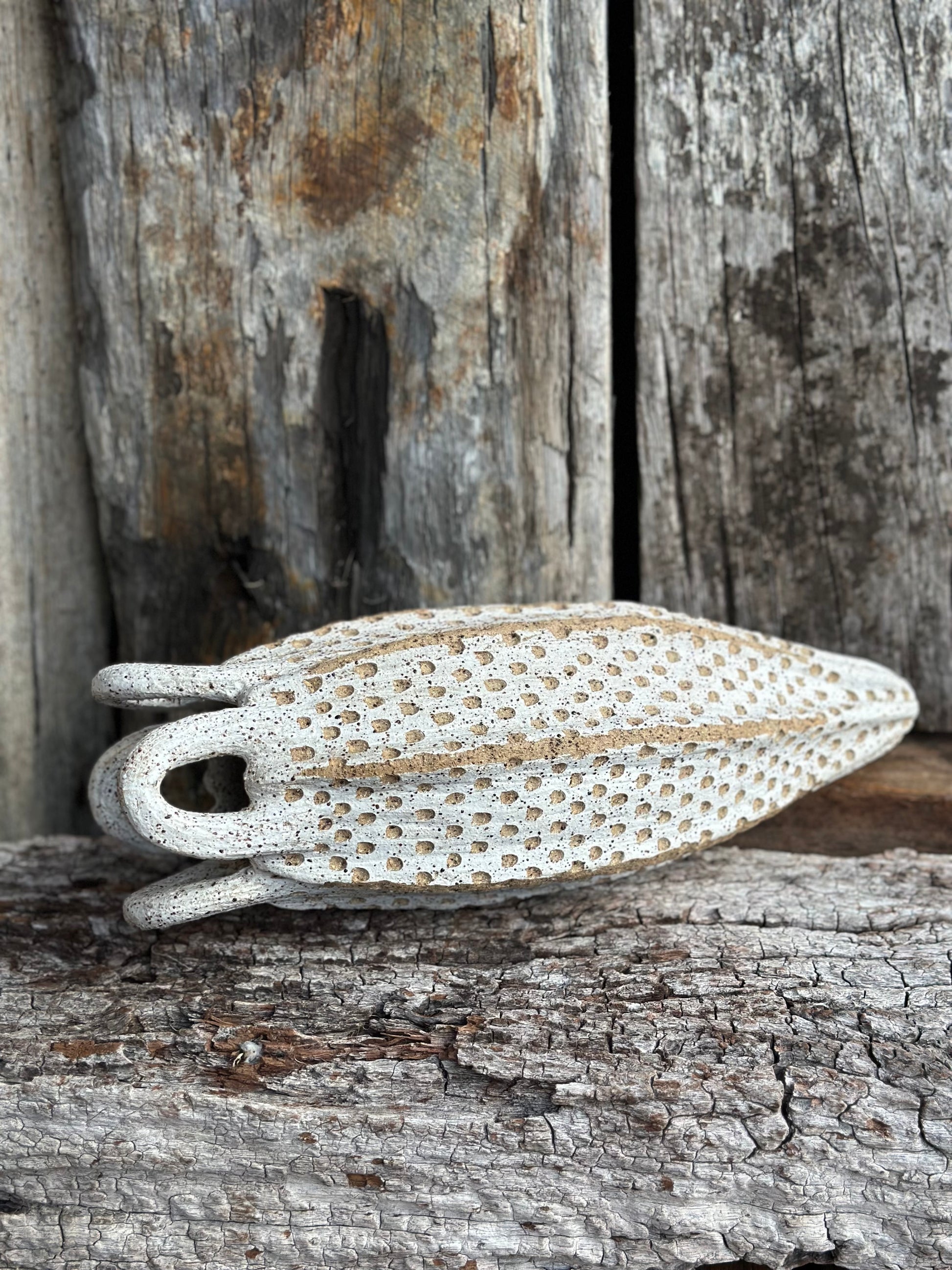 Side angle of textured ceramic vessel, white-washed peaks revealing earthy iron mottling beneath.