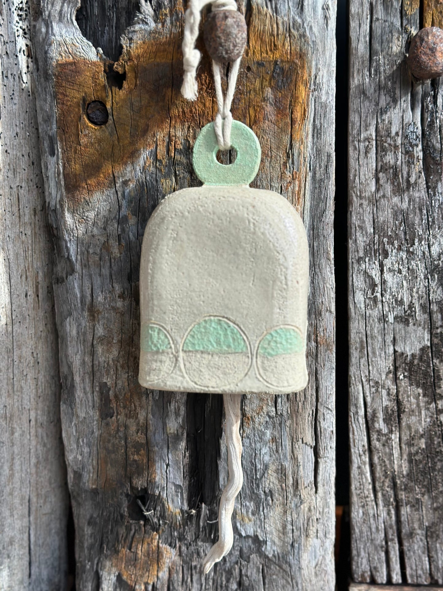 Detail of textured white raku clay and mint motif on handmade stoneware bell, highlighting organic surface