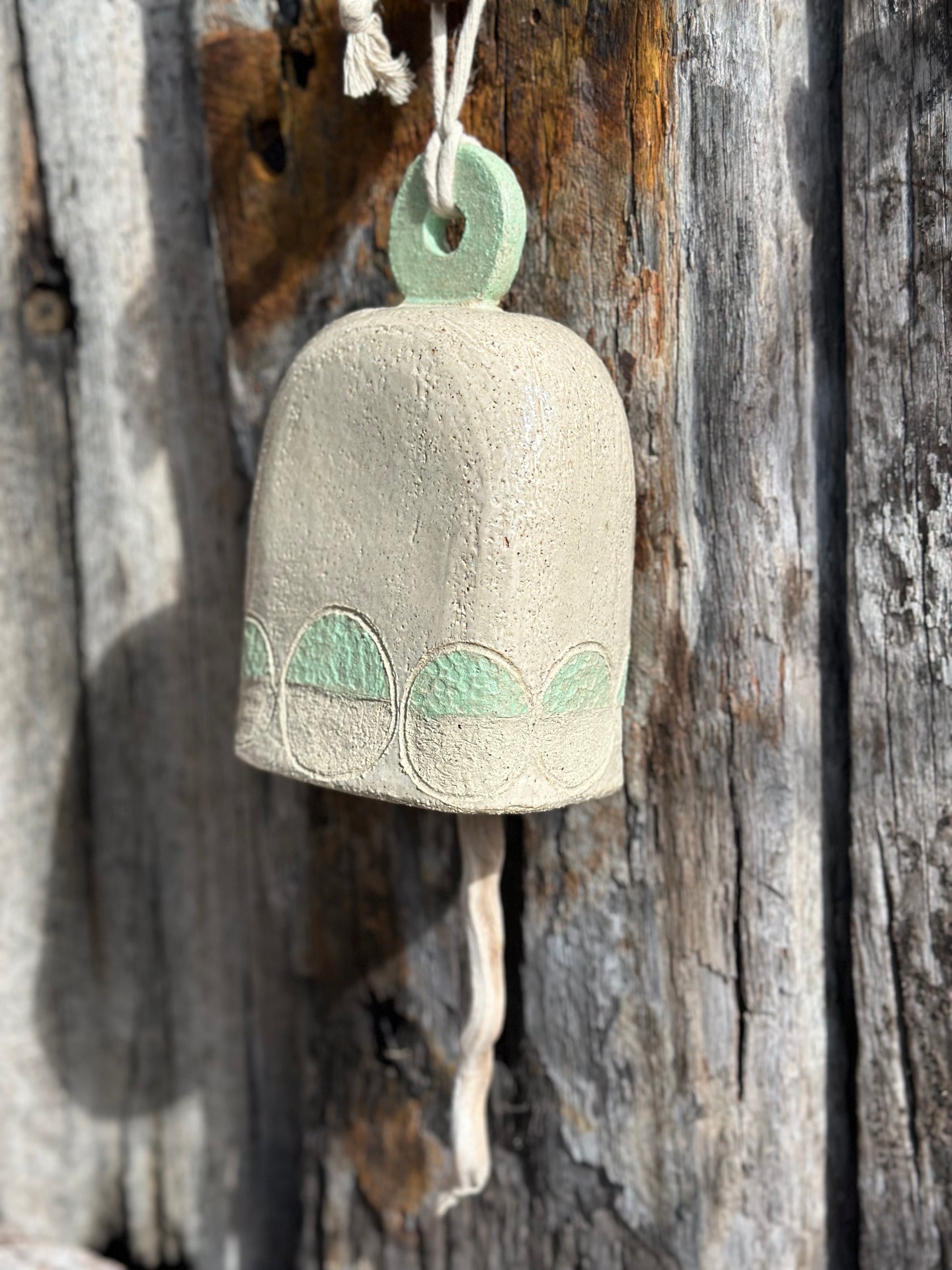 Stoneware bell hanging from a tree branch, showing natural texture and soft outdoor light
