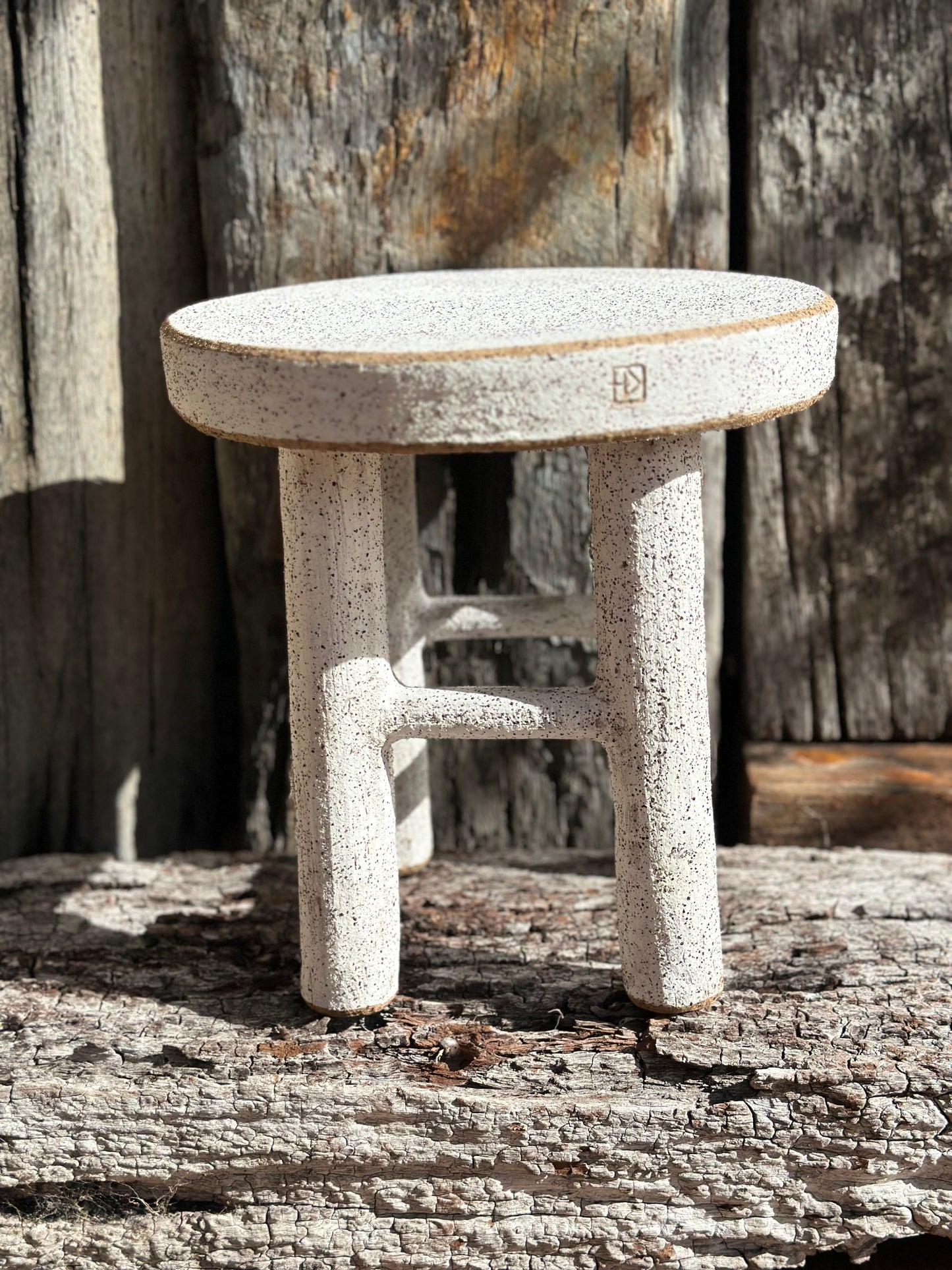 Handmade ceramic stool with four legs, white underglaze, and exposed clay rim