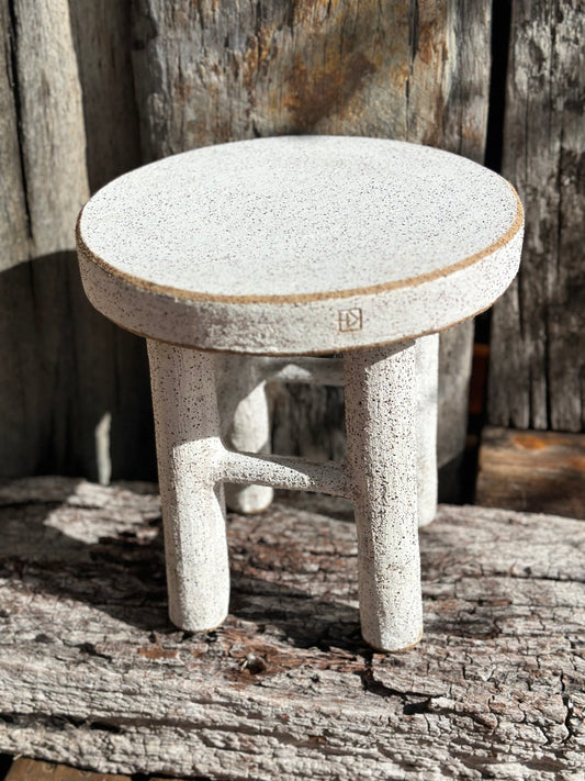 Handmade ceramic stool with four legs, white underglaze, and exposed clay rim Handmade ceramic milking stool with white underglaze and exposed raw clay rim, shown in full view