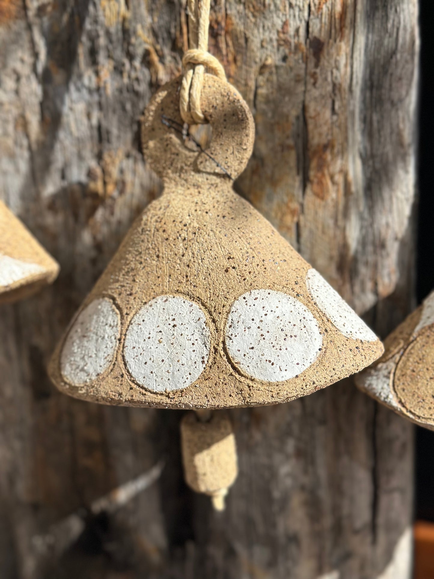 Textured stoneware bell form with subtle mid-century modern patterning, hanging against timber backdrop