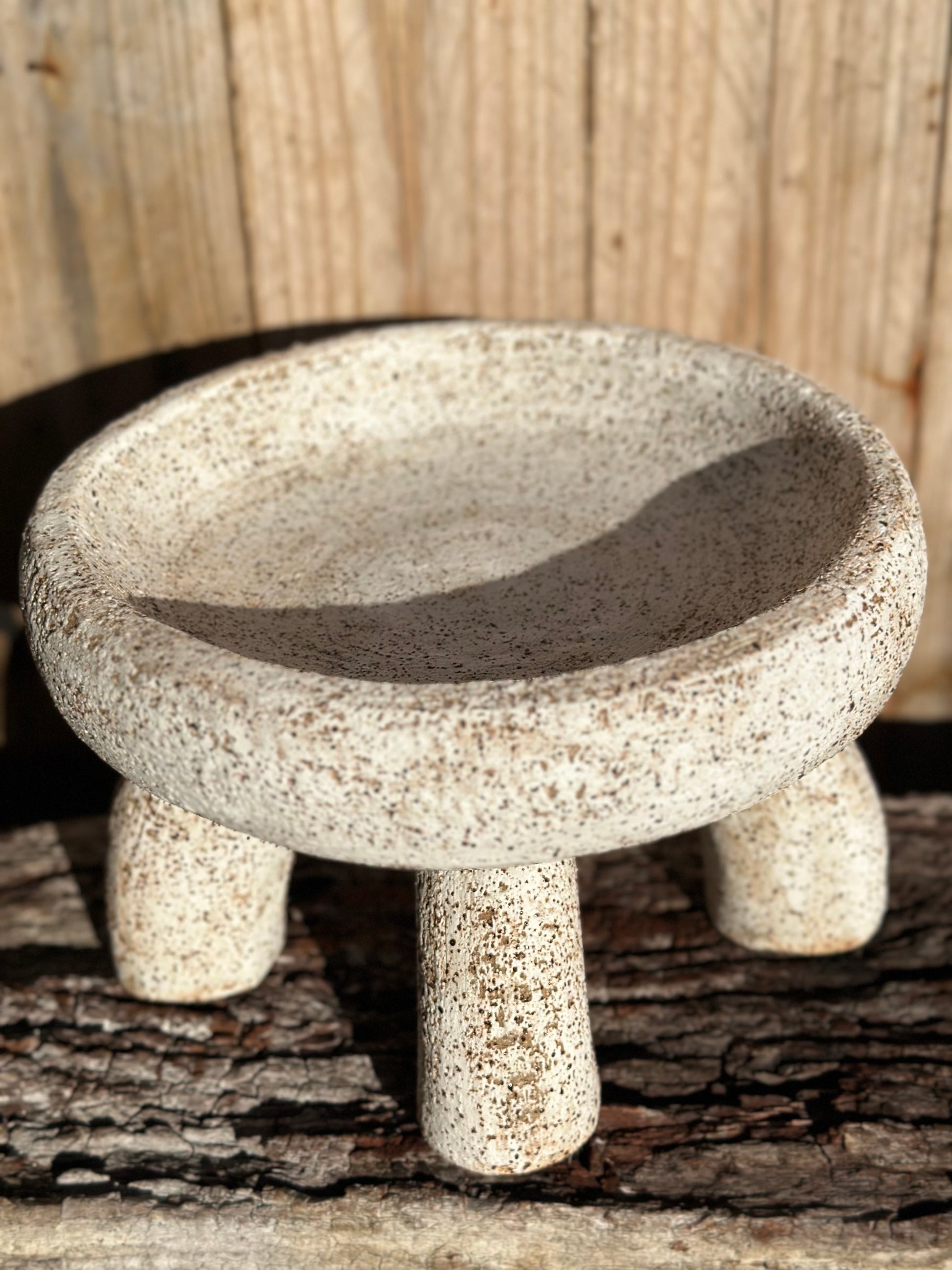 Sculptural ceramic bowl resting on four arched tubular supports, finished in brushed white glaze revealing gritty stoneware texture