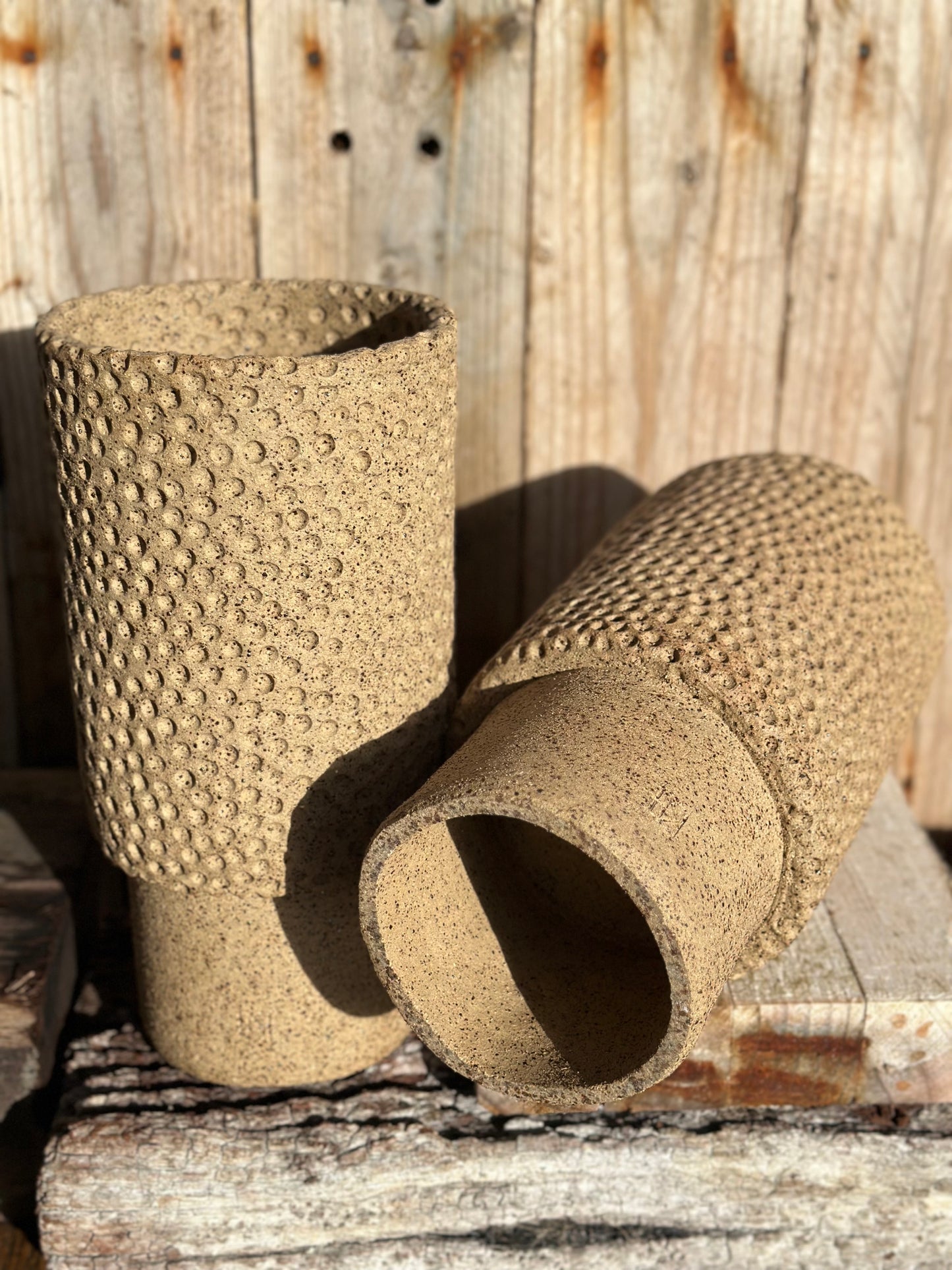 Pair of cylindrical stoneware vessels with stippled relief texture and smooth lower bases on timber surface
