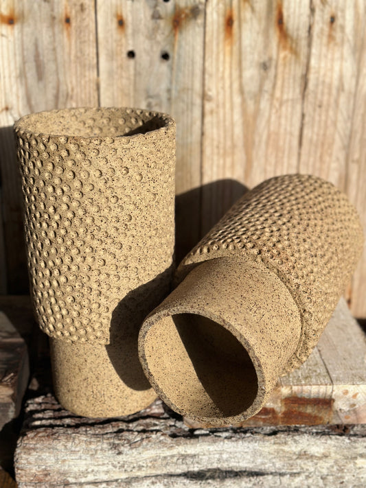 Pair of cylindrical stoneware vessels with stippled relief texture and smooth lower bases on timber surface