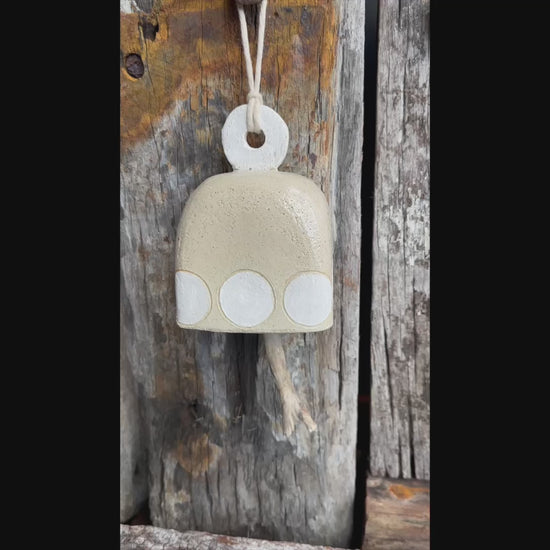 Sculptural ceramic bell in natural glaze with white circular detailing and driftwood striker, suspended on flax rope